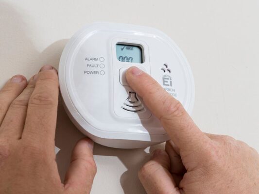 Close up of someone pressing the button on a carbon monoxide alarm to test it