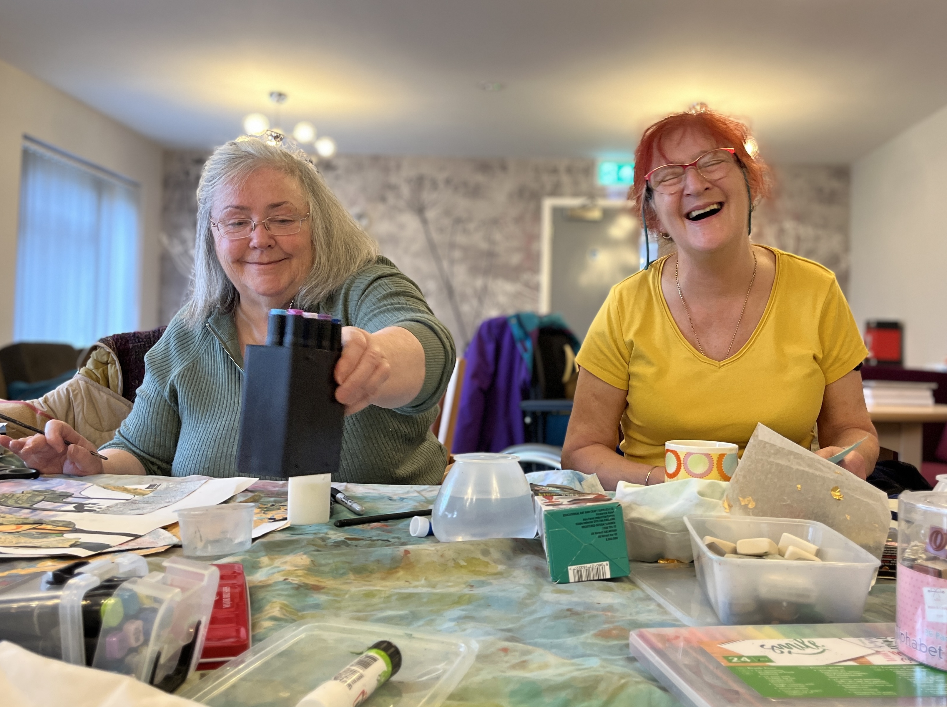 Two older females laughing and enjoying creating art together