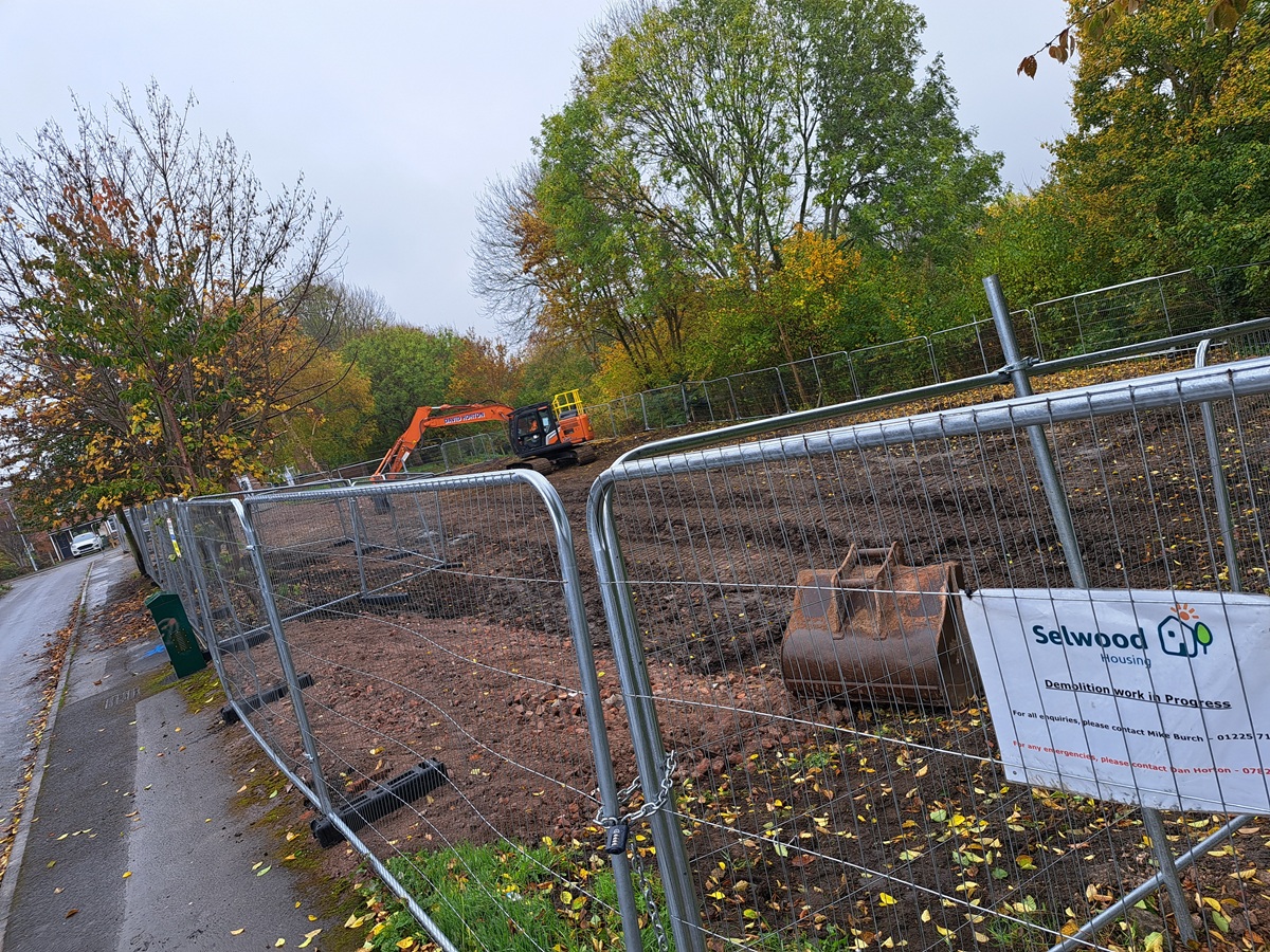Digger in fenced off area clearing away debris from demolition of flats