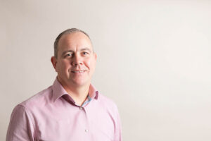 Photo of executive team member Darren Bird, smiling and looking to camera in front of cream coloured background.