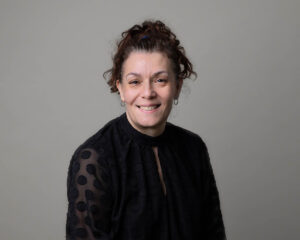 Image of group director Ria Bristow smiling at camera in front of a grey coloured background.