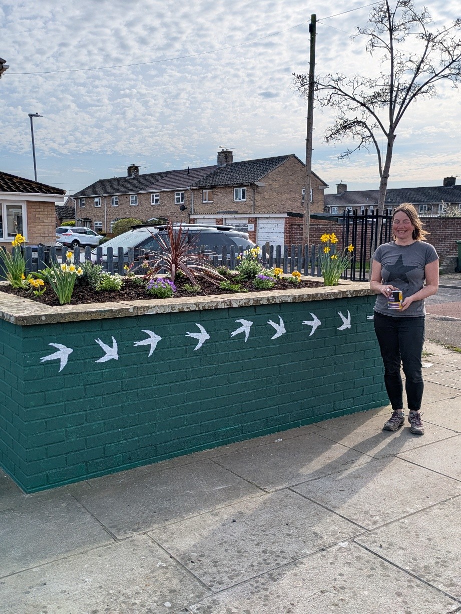 A member of staff stands proudly in front of a refurbished planter
