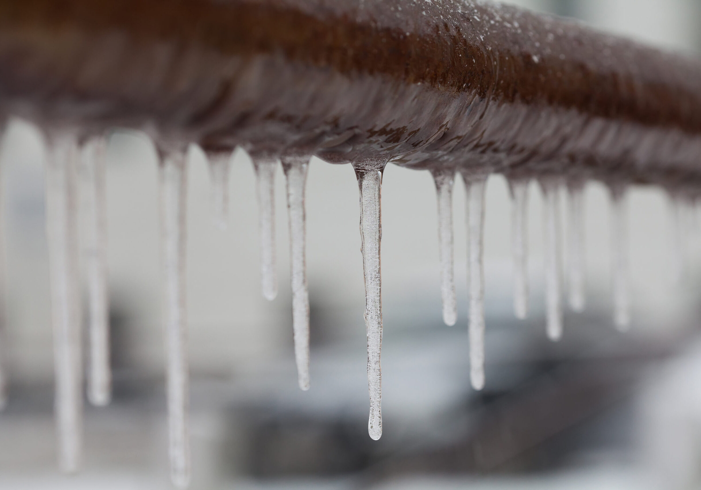 Icicles hanging from a brown pipe. Frozen water and metal surface, winter time concept. selective focus shallow depth of field photo
